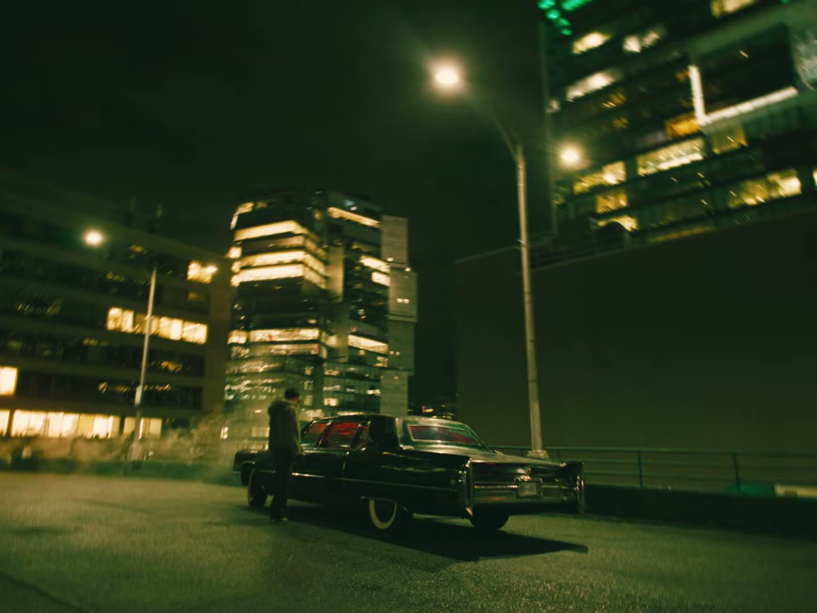 A black car parked on a rooftop at night under sodium street lights, Vancouver towers behind, from Ruinas