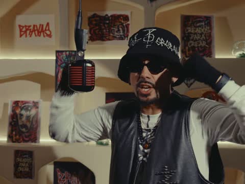 RAW 001, frame 03: Rapalavein in a black bucket hat and sunglasses at the microphone, BRAVAS tag on the wall behind