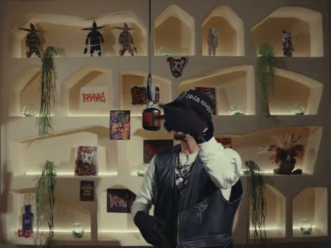 RAW 001, frame 05: Rapalavein with a hand over his face in front of the lit shelves