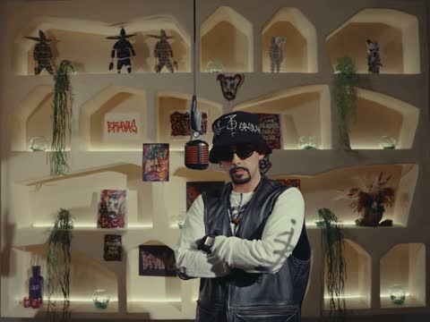 RAW 001, frame 10: Rapalavein standing with arms crossed in front of the shelf wall