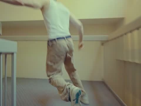RAW 002, frame 01: a man in a white tank top walking away down a bright corridor