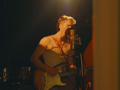 RAW 002, frame 09: the singer with a guitar at the microphone in the dark studio