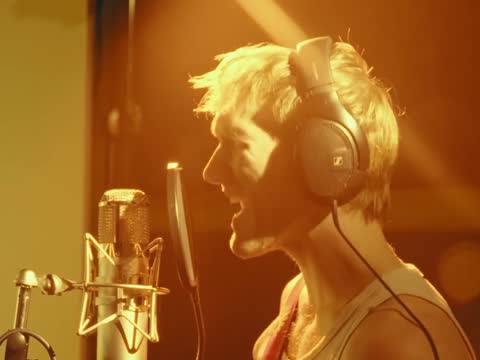 RAW 002, frame 12: the singer shouting into the microphone in amber light