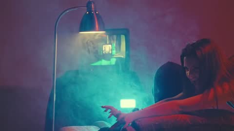 RUINAS BTS, frame 02: a woman leaning over an armchair under a lamp in teal light