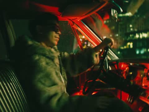 RUINAS, frame 01: a man in a fur coat driving a car lit red at night