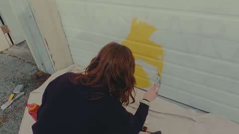 SPCA, frame 05: a woman painting a yellow shape on a white wall